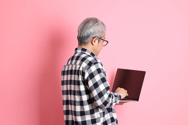 Взрослый азиат 40-х годов прячется на розовом фоне в повседневной одежде. - Фото, изображение