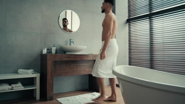 Naked bare sexy Latina Hispanic Indian man going walking in bath with white towel on hips washes face with warm water in bathroom sink cleaning facial skin looks at mirror reflection hygiene washing - Footage, Video