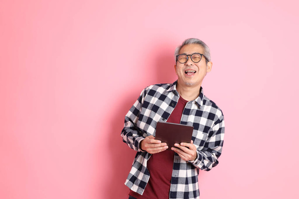 Взрослый азиат 40-х годов прячется на розовом фоне в повседневной одежде. - Фото, изображение