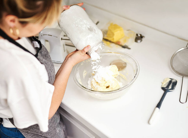 Agregue más harina si la mezcla está demasiado húmeda. Foto retrospectiva de una joven mujer agregando harina a su masa - Foto, imagen