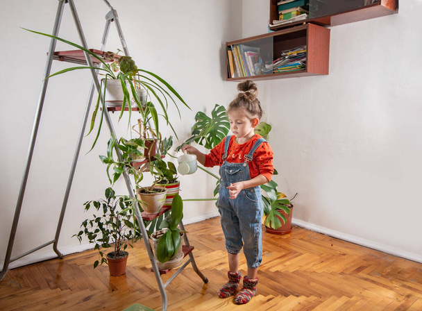 Little girl watering plants in a room with home plants. Plant care and sustainable living - Фото, зображення