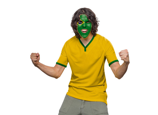 Soccer fan man with jersey and face painted with the flag of the Brazil team screaming with emotion on white background. - Photo, image