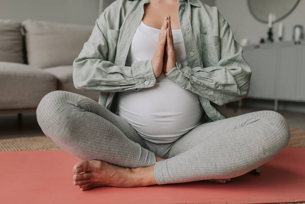 Закрите тіло вагітної жінки одягає затишні активи і медитує, сидячи в позі лотоса, робить вправи для дихання розважними. Йога, підтримуй добре самопочуття під час концепції вагітності. Висока якість - Фото, зображення