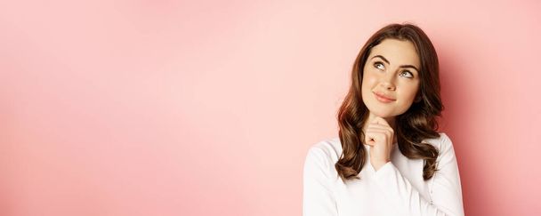 Close up portrait of coquettish smiling woman, glamour girl thinking, looking thoughtful, standing over pink background. - Photo, Image