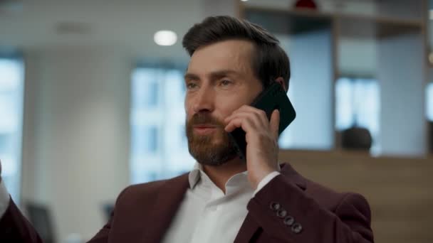 Успешный бизнесмен разговаривает по телефону в офисе крупным планом. Элегантный лидер, объясняющий детали деловому партнеру. Позитивный работник разговаривает на смартфоне. Концепция корпоративного стиля  - Кадры, видео