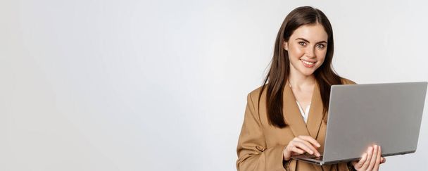 Portrét firemní ženy pracující s notebookem, usmívající se a vypadající asertivně, bílé pozadí. - Fotografie, Obrázek