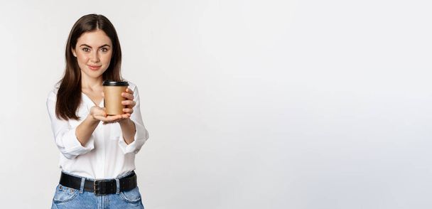 Image of modern woman, office lady holding takeaway coffee cup and smiling, standing over white background. - Foto, imagen