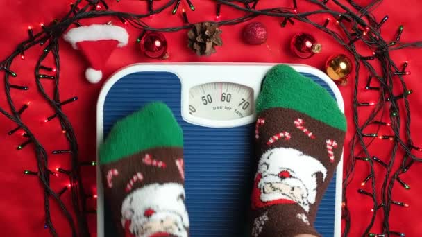 Žena ve vánočních ponožkách stojí na váze, váží se po nenasytnosti během svátků. - Záběry, video