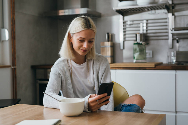 woman using mobile phone in her kitchen - Foto, Bild