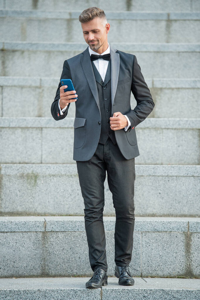elegant man in bowtie suit outdoor. businessman man using phone. man boss chat on smartphone. - Photo, image