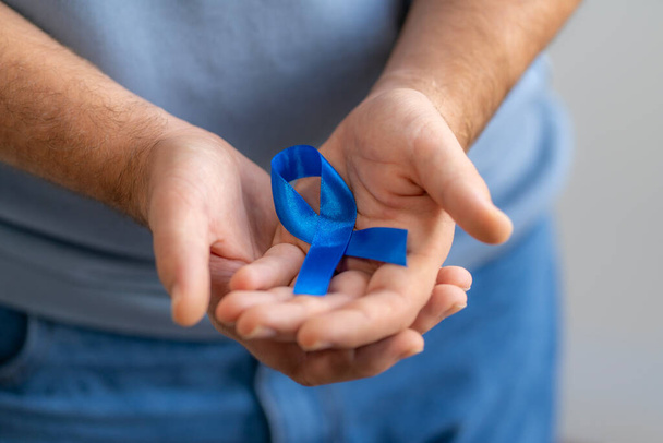 manos masculinas sosteniendo una cinta azul que simboliza el cáncer de próstata y la campaña de concienciación sobre la salud de los hombres. - Foto, Imagen