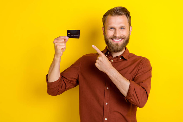 Portrait of cheerful nice person indicate finger hand hold plastic debit card isolated on yellow color background. - Fotografie, Obrázek