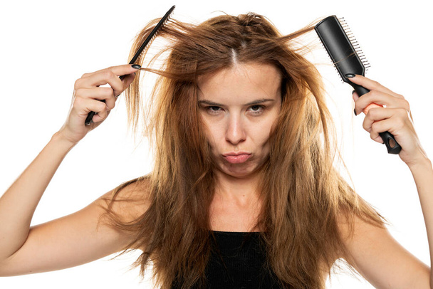 portrait of a young unhappy woman brushing her messy long hair on a white background. - Photo, Image