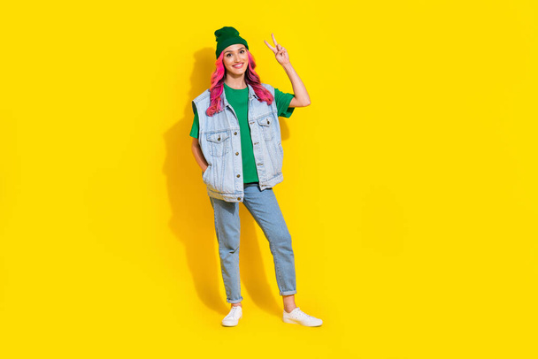 Full length photo of adorable sweet lady wear jeans waistcoat smiling showing v-sign isolated yellow color background. - Фото, изображение