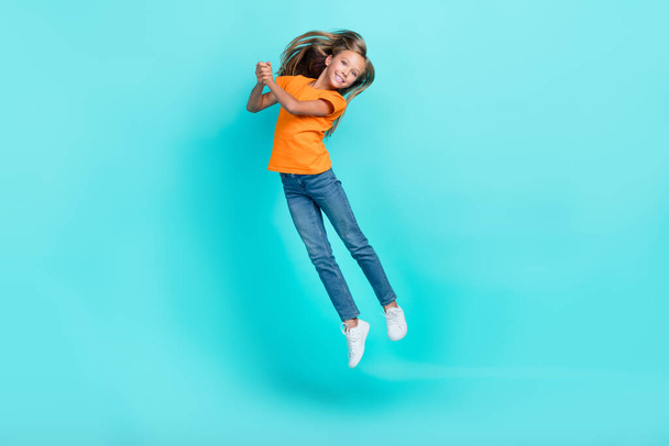 Full body size photo of cute little pretty schoolgirl wear orange t-shirt jumping air trampoline new sneakers shopping carefree isolated on cyan color background. - Fotó, kép