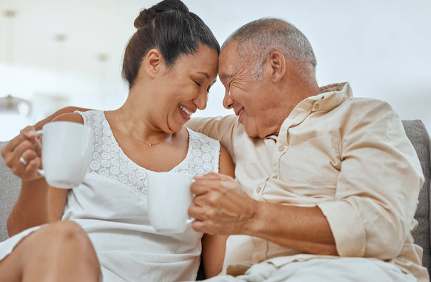 Αγάπη, καφές και ηλικιωμένο ζευγάρι χαλαρώνουν σε έναν καναπέ, πίνοντας καφέ και αγκαλιάζοντας σε ένα σαλόνι. Χαρούμενη οικογένεια, συνταξιοδότηση και τσάι με ώριμο άνδρα και γυναίκα χαμόγελο, ευτυχισμένη και απολαμβάνοντας ρομαντικό διάλειμμα. - Φωτογραφία, εικόνα