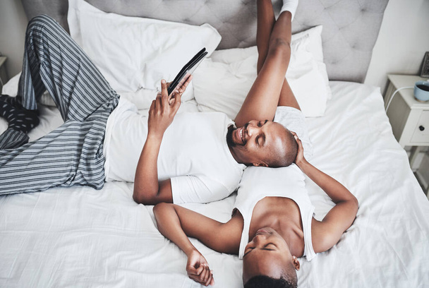 Entspannung war noch nie so entspannt wie heute. ein glückliches junges Paar, das zu Hause ein digitales Tablet im Schlafzimmer benutzt - Foto, Bild