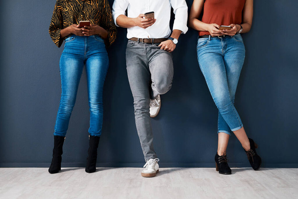 We are millennials. an unrecognizable group of businesspeople standing against a gray background in the studio and using their cellphones - Photo, Image