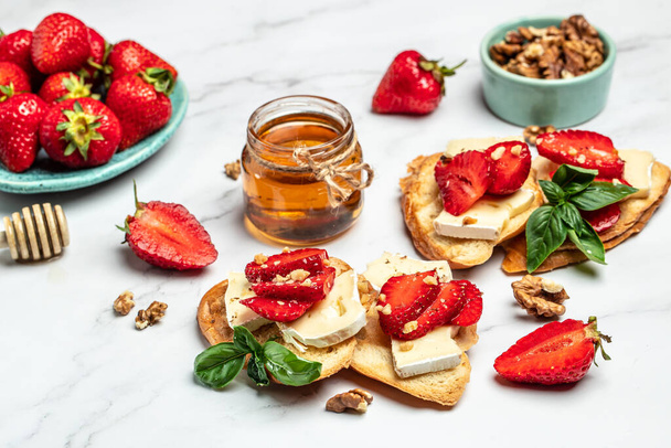Two toasts or bruschetta with trawberries, cheese camembert nuts and honey. Summer breakfast. Healthy, clean eating. Vegan or gluten free diet. - Photo, Image