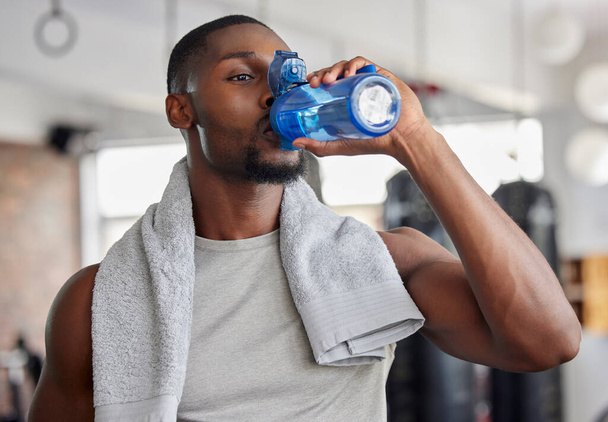 Water, drink and fitness with a sports man in a gym for exercise while taking a break to hydrate. Workout, training and drinking with a male athlete taking a sip from a bottle after his routine. - Foto, afbeelding
