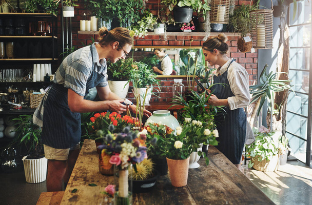Nuestro lugar de trabajo es nuestro lugar feliz. dos floristas jóvenes regando flores y trabajando juntos dentro de su vivero de plantas - Foto, imagen