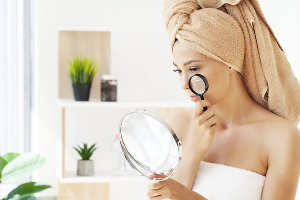 Beautiful face of a young woman with clean fresh skin holding a magnifying glass. - Photo, Image
