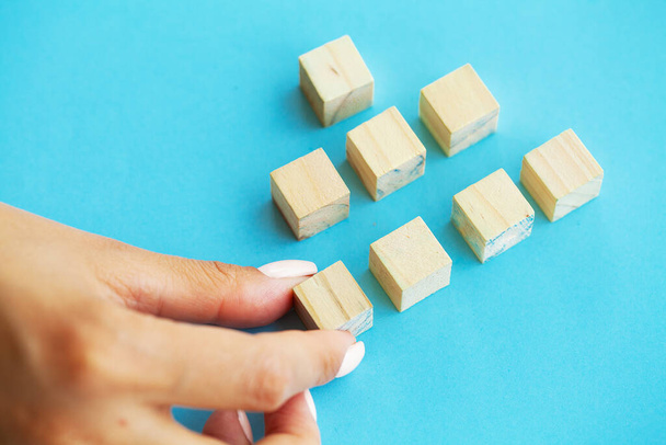 Wooden blocks with a human hand placing one cube at the top on blue background - Photo, image