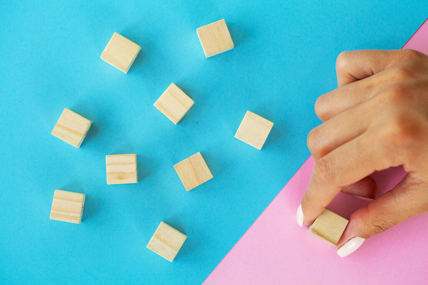 Mão feminina organizando bloco de madeira vazio e espaço de cópia em fundo azul e rosa. - Foto, Imagem