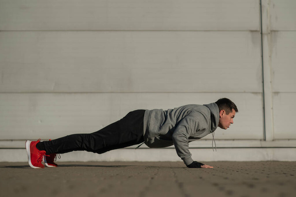 A man in a hoodie jumps while doing push-ups outdoors - Фото, зображення