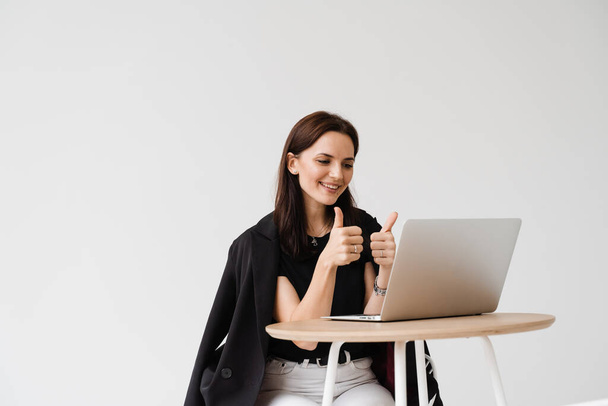 Cheerful woman showing thumbs up to her colleagues and friends on video meeting. Happy girl with works on laptop and rejoices in the implementation of successful project - Φωτογραφία, εικόνα