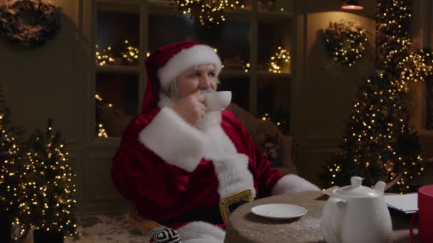 Санта-Клаус сидит на заднем дворе, наслаждается своим свободным временем, расслабляется и пьет чай, наслаждаясь уютным вечером, медленным движением. - Кадры, видео