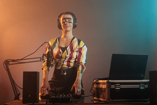 Happy żeński wykonawca pracuje jako DJ z gramofonami, mieszając muzykę techno z basem i sprzętem audio. DJ kobieta gra piosenki na mixer, stojąc nad kolorowym tle z dymem. - Zdjęcie, obraz