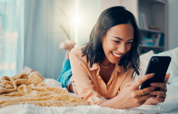Glück, soziale Medien und Frau im Bett mit Telefon, lächelnd, lachend und entspannt zu Hause. Meme, online und Mädchen auf dem Smartphone SMS, Chat und Surfen im Internet im Schlafzimmer, um am Wochenende zu entspannen. - Foto, Bild