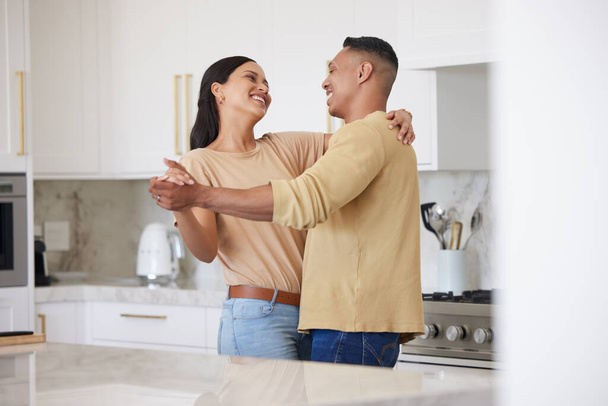 Love, smile and couple dance in kitchen, celebrating anniversary and bonding. Happy, man and woman dancing, romance and affection, carefree or playful people having fun spending time together in home. - Foto, afbeelding