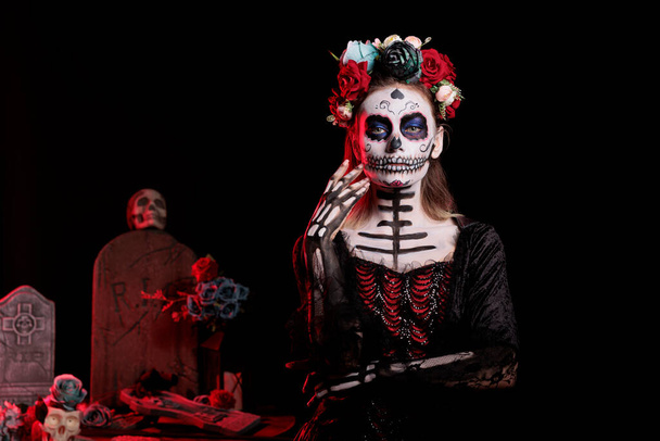 バラと花のヘッドバンドを身に着けて、黒の衣装とカトリーナ頭蓋骨のボディアートで死んだの怖い女神。スタジオでハロウィンでdios de los muertosメキシコの伝統を祝う. - 写真・画像