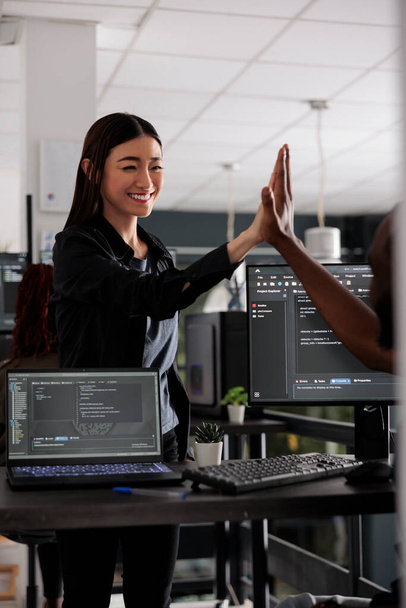 Diverse successful web developers celebrating code compiling, doing highfive hand gesture after system development. Coders analyzing algorithm and creating app server interface in data office - Photo, Image