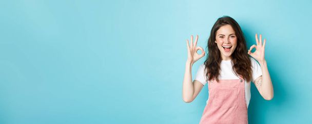 Very well, alright. Excited smiling brunette guy say yes, showing okay signs and agree with you, praising good job, standing happy against blue background. - Photo, Image