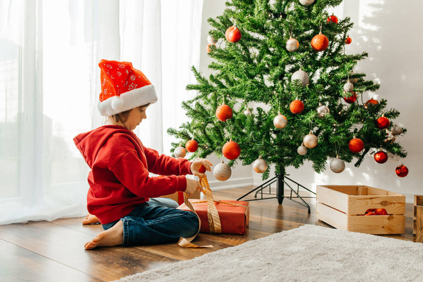 Año Nuevo y Navidad. El chico desata el lazo y abre la caja con un regalo de Navidad. - Foto, Imagen