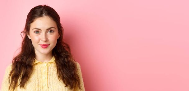 Close up de jovem modelo feminino de 20 anos com bonito feminino compõem, sorrindo e olhando esperançoso para a câmera, de pé contra o fundo rosa. - Foto, Imagem