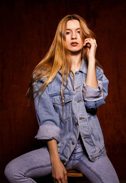 Young adult woman sitting on a chair in a studio looking at camera wearing all denim looking at camera. - Foto, Imagem
