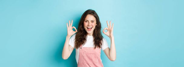 Very well, alright. Excited smiling brunette guy say yes, showing okay signs and agree with you, praising good job, standing happy against blue background. - Foto, afbeelding