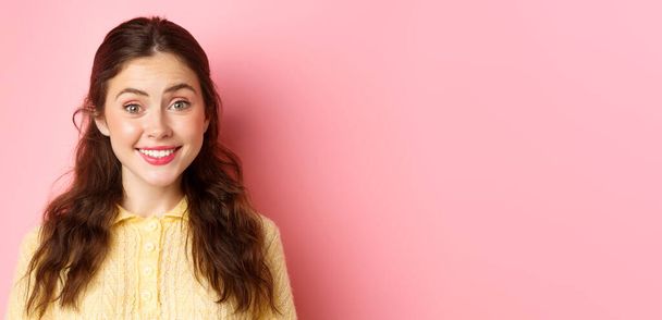 Close up of cute brunette lady smiles at camera, trying to make friendly and polite face, stands against pink background. Copy space - Photo, Image