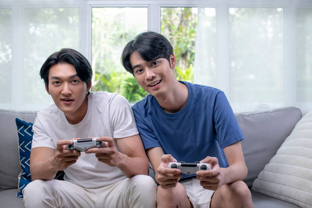 Asian gay lgbt men couple play video games at home, males having funny happy moment together on sofa in living room. - Photo, Image