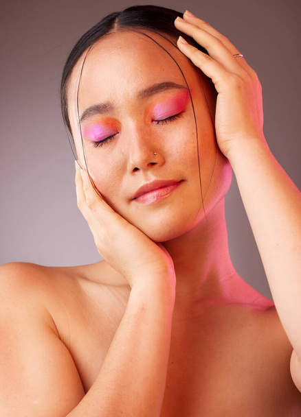 Eyeshadow, asian and beauty woman with hands on face pose with pink and orange cosmetics. Funky, trendy and colorful fashion makeup model for Gen Z cosmetic style on grey studio background - Photo, image
