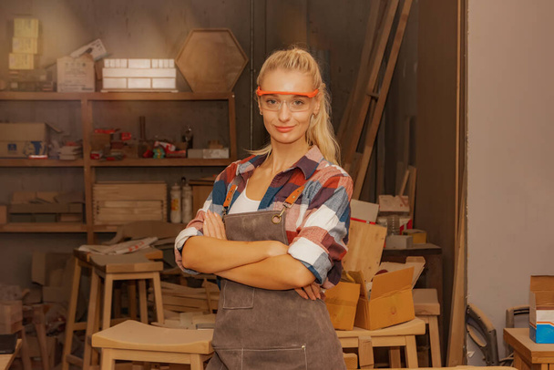 Muotokuva nainen puuseppä yllään turvalasit huonekalujen valmistus tehdas seisoo puunjalostus työpaja tilalla työpaja ylpeänä katsot älykäs kamera, kädet ristissä kädet. - Valokuva, kuva
