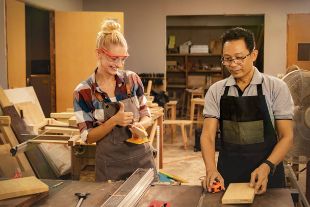 白人女性学生親指アップシニアアジアの大工の先生は、木材加工機のツールを安全かつ理解しやすい教え,木工の慎重なデモンストレーションを示します. - 写真・画像