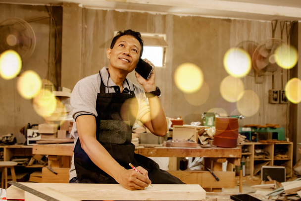 Vanhempi aasialainen puuseppä työntekijät käyttävät älypuhelimia ottaa tilauksia asiakkailta, järjestää puiset huonekalut mukaan asiakkaiden vaatimukset huolellisesti, ystävällinen ilmapiiri. - Valokuva, kuva