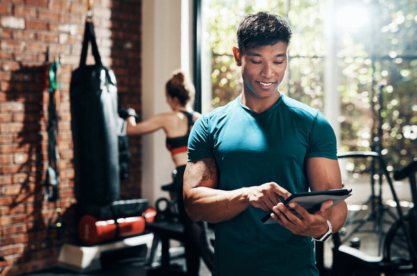 Modern fitness uygulamaları sağ olsun. Spor salonunda dijital tablet kullanan yakışıklı genç bir sporcu ve arka planda spor eşi. - Fotoğraf, Görsel