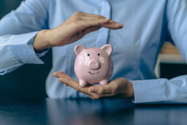 Die Hand der Frau schützt ein Sparschwein und spart mit einem Stapel Münzen Geld. Schritt in ein erfolgreich wachsendes Geschäft Sparideen - Foto, Bild