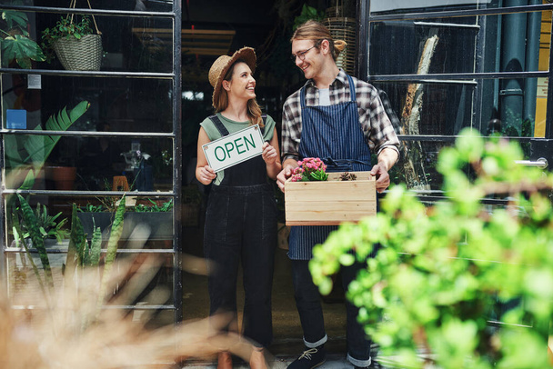 Tule katsomaan ympärillesi. kaksi nuorta yrittäjää seisomassa kukkakauppansa sisäänkäynnillä yhdessä ja pitämässä ruukkutarvikkeita - Valokuva, kuva